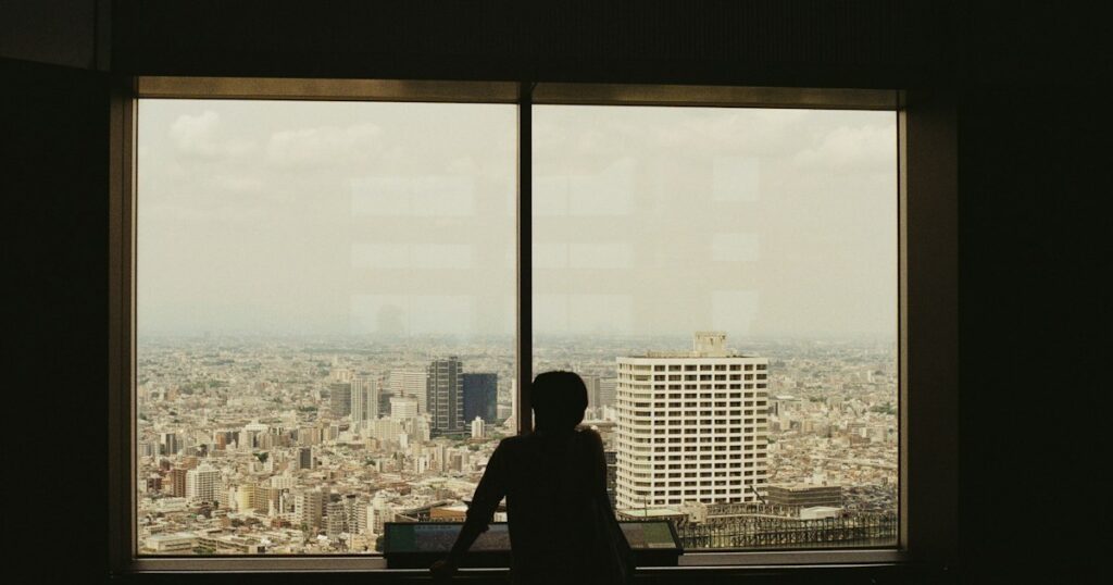 Silhouet van iemand die door een groot raam over de stad uitkijkt