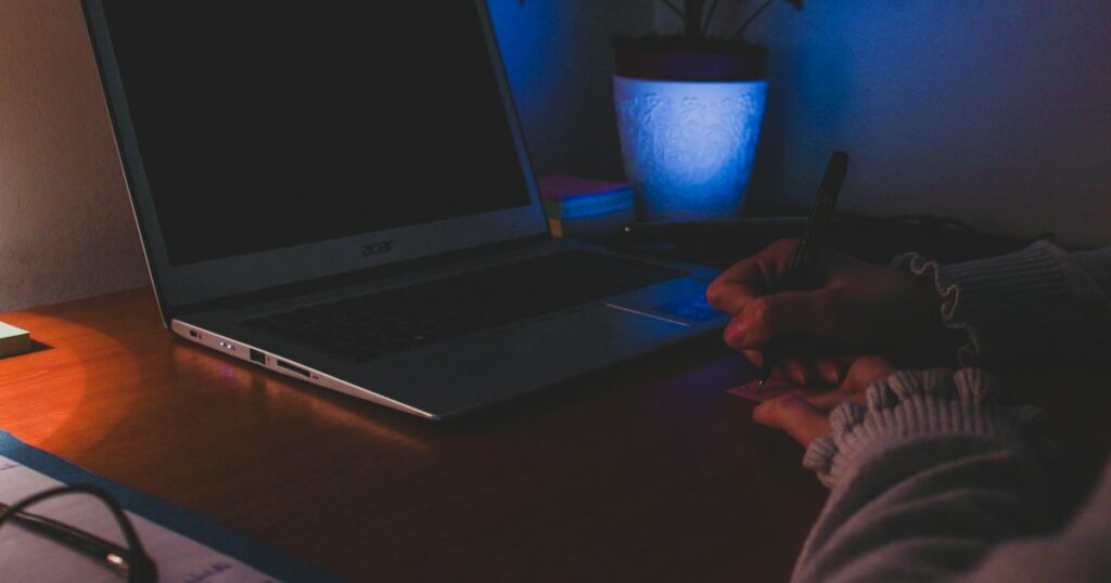 Handen van iemand die in de avond aan een bureau achter een laptop werkt