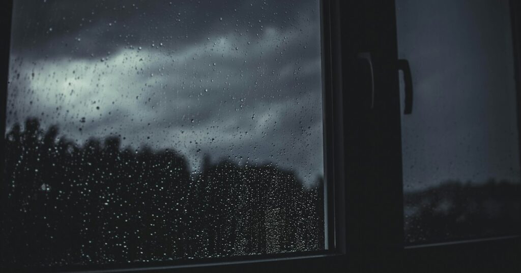 Regendruppels op een raam met een donkere, bewolkte lucht erachter